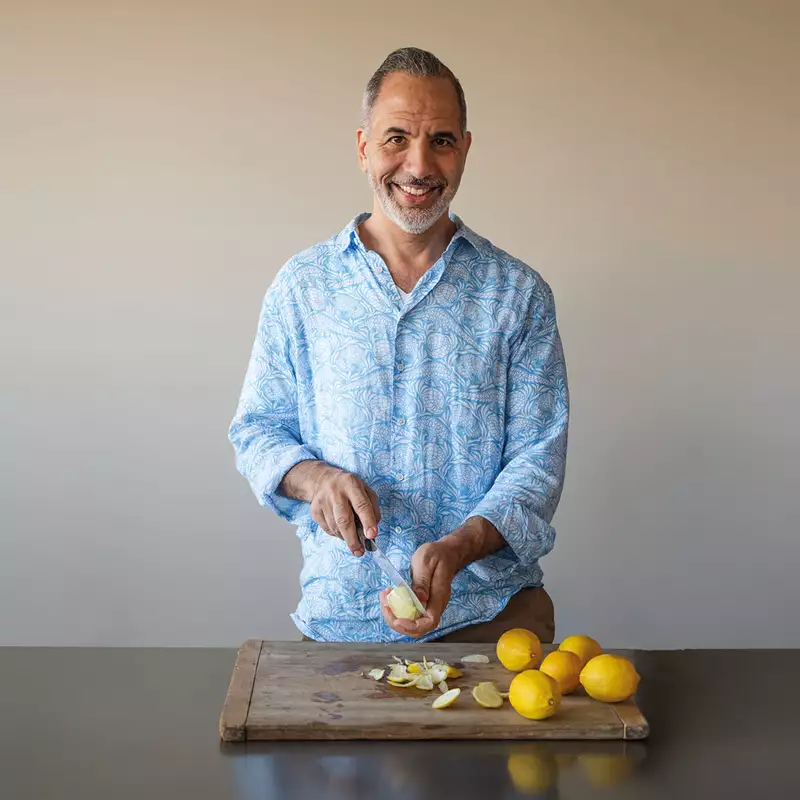 Yotam Ottolenghi wearing a light blue shirt cutting lemons on a wooden board