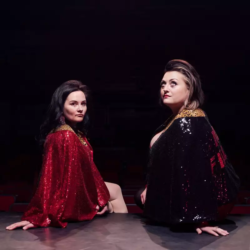 Kiri Pritchard-McLean and Rachel Fairburn sat on a stage wearing glittery outfits