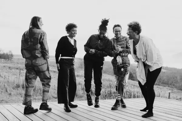 Black and white photograph of five people stood up laughing and smiling