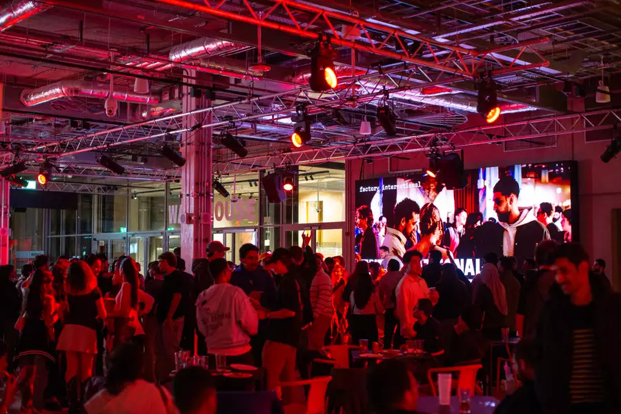 A crowd of people mingling in the Social under red lighting. Some are sat down drinking.