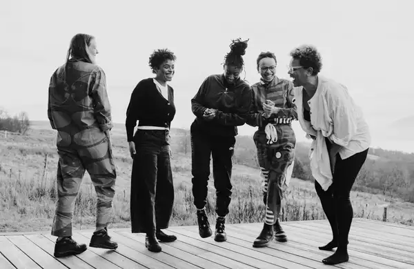 Black and white photograph of five people stood up laughing and smiling