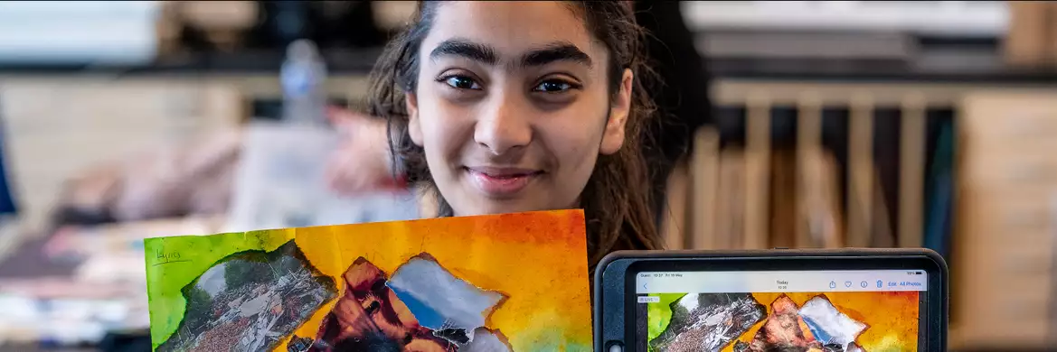A child holding up their artwork and smiling