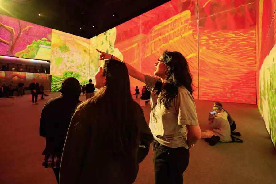 An image from David Hockney: Bigger & Closer (not smaller & further away) showing two people pointing upwards at the exhibition