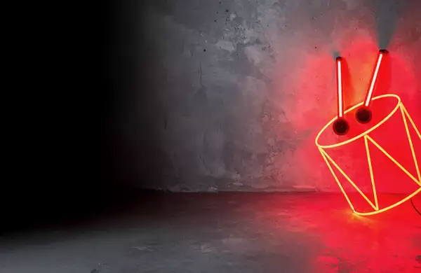 Neon red drum sign with drumsticks leaning against a concrete wall.