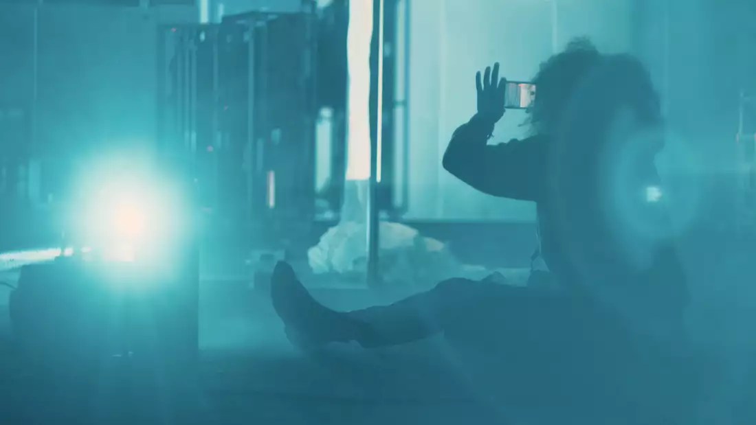 Juliet Ellis taking a photo sat on the floor, in a blue-lit, smoky environment.