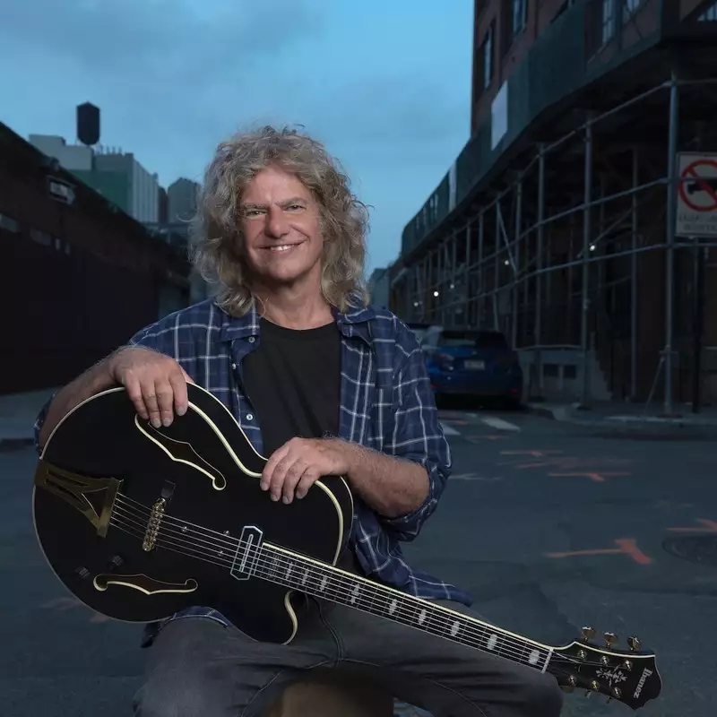 Pat Metheny with a guitar on a street outside at night