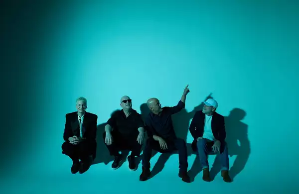 Four members of Pixies wearing all black on a bright turquoise background