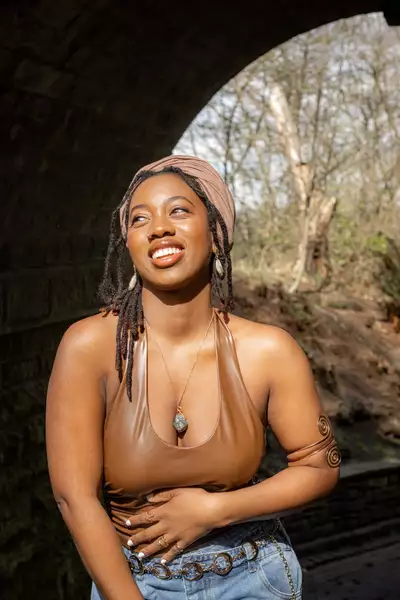 Tsana stood outside in a forest wearing a brown top smiling