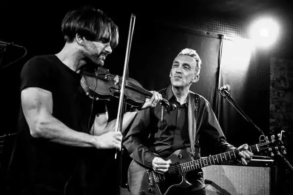 Black and white photograph of Justin Adams and Mauro Durante playing guitar and violin on stage