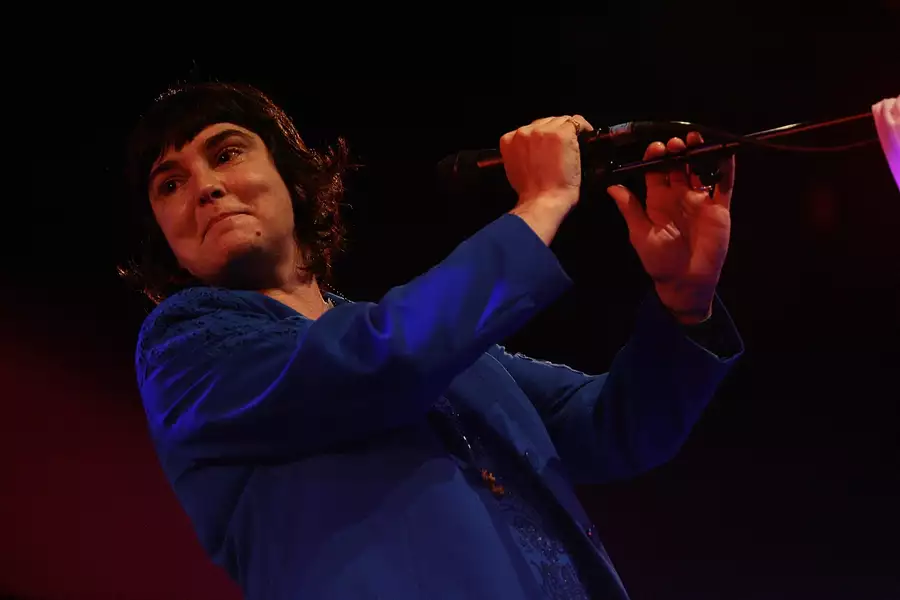 Sinéad O’Connor wearing a dark blue jacket singing into a microphone