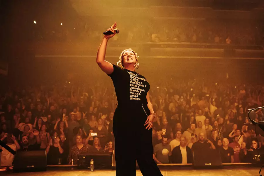 Jenna G performing on stage at the Southbank, in front of a large crowd. The lighting is yellow.