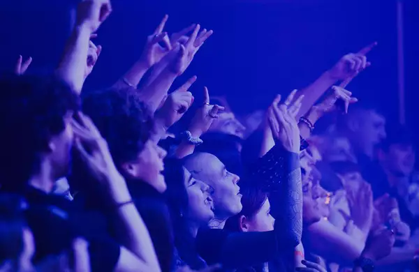 A crowd of people cheering and filming over the barrier in the Warehouse at Aviva Studios. The lighting is blue.