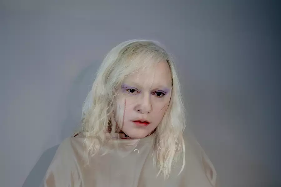 Headshot of Anohni with blonde hair, stood in front of a white wall
