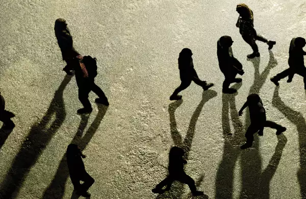 Aerial view of people walking with long shadows cast on a textured ground.