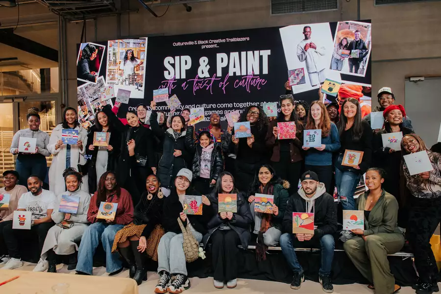 A large group of people are posing together at a Sip & Paint event in the Social, holding up their colourful artworks. The large screen reads “SIP & PAINT with a twist of culture” and features event branding by “Cultureville & Black Creative Trailblazers.”