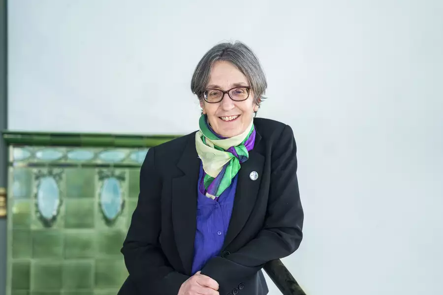 Helen Pankhurst smiling in front a green tiled wall