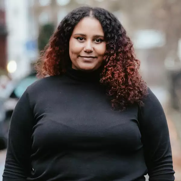 Square headshot of Fauziya Johnson stood outside wearing a black top. The background is blurry.