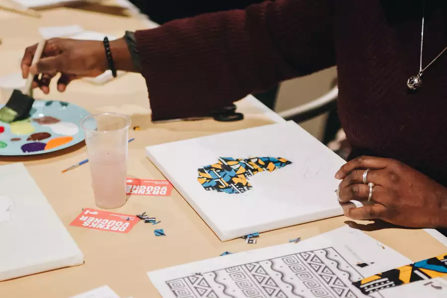A person is working on a mixed-media art project involving painting and patterned fabric cutouts on a canvas.