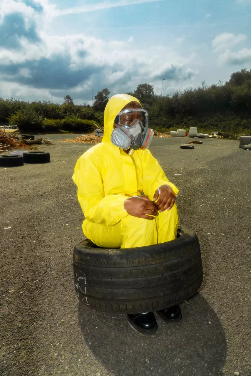 A person in a yellow hazmat suit and face mask sits inside a car tyre outside.