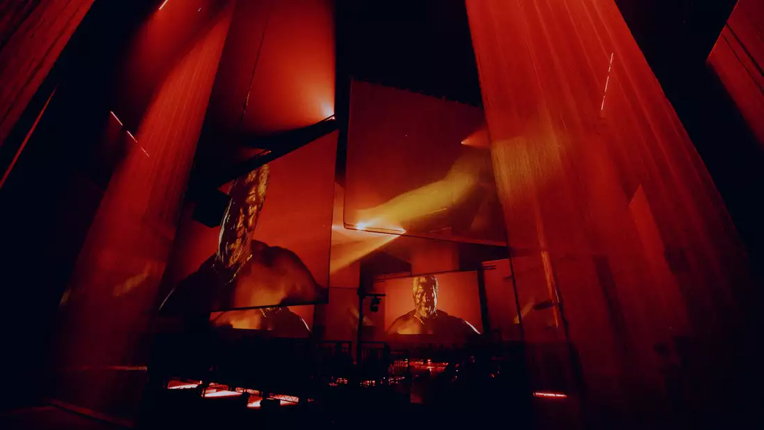 The set of A Symphony of Flesh and Bones in the Warehouse, showing projections on large screens and pieces of fabric. The screens show her father and the lighting is red.