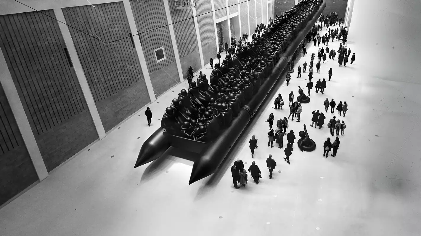 Ai Weiwei's Law of the Journey artwork, showing a crowd of people surrounding a huge, inflatable migrant boat in a big warehouse