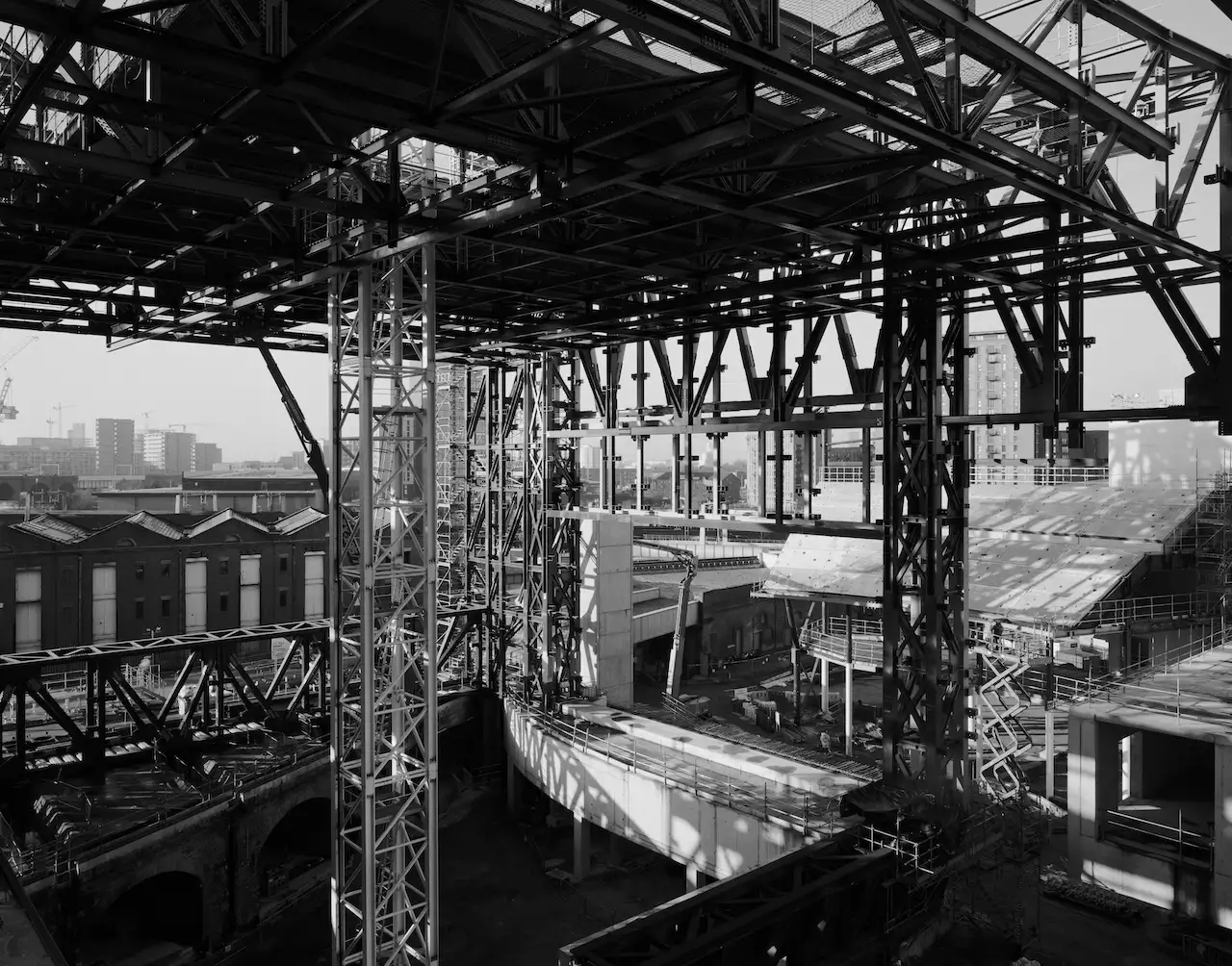 Black and white photograph of the skeleton of Aviva Studios, with cranes and Manchester's skyline