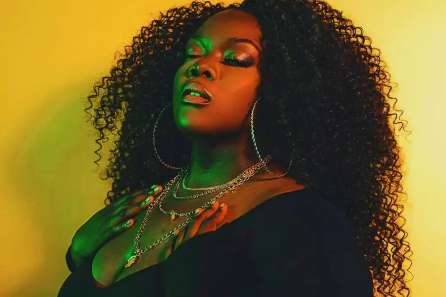 Dija Bhule looking up with eyes close bathed in blue light and against a.yellow backdrop