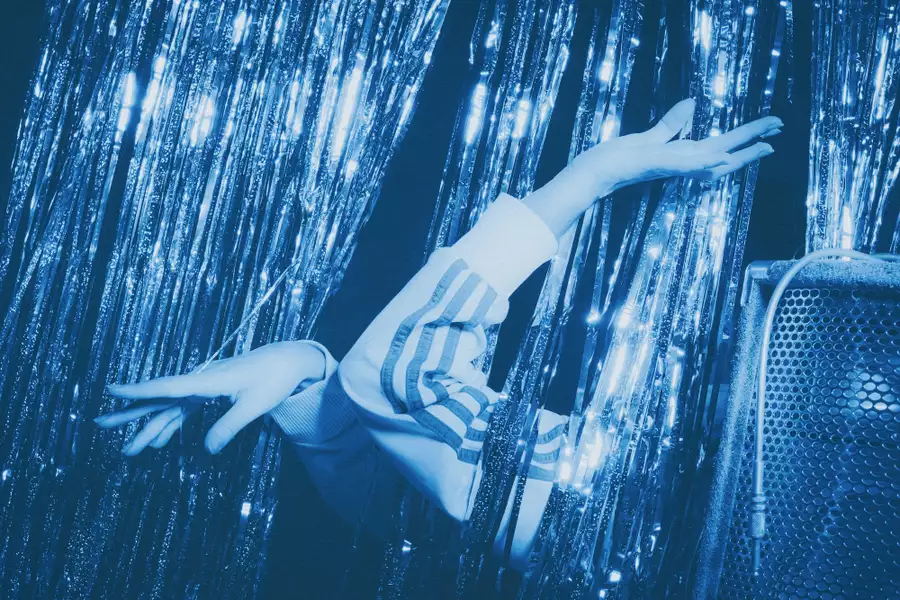 Person dancing among shimmering blue streamers beside a speaker.
