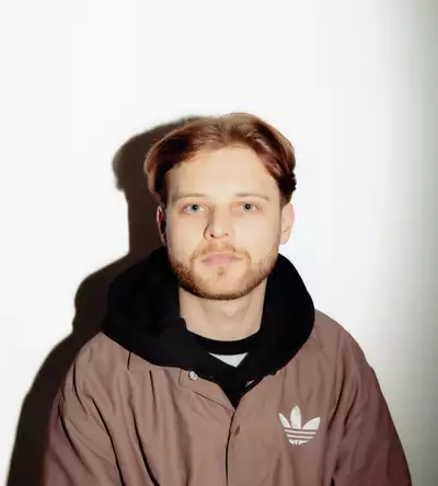 Oscar Cloud wearing a back hoodie and brown Adidas jacket, on a white background