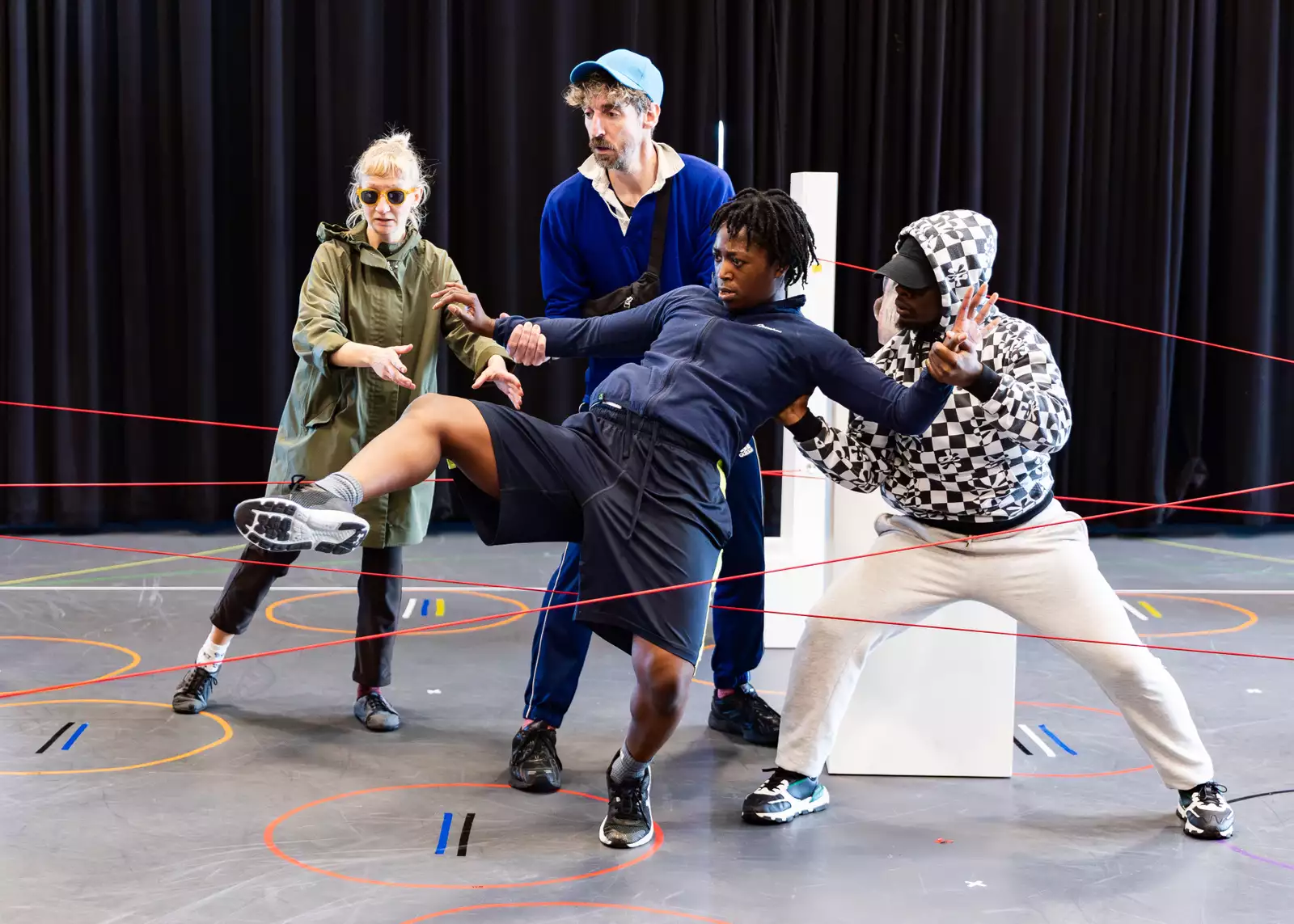 Four people dance around lasers and plinths in the rehearsal room