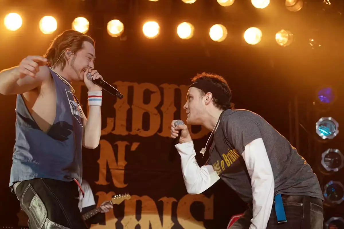 A still from California Schemin' showing two men on stage singing into a microphone