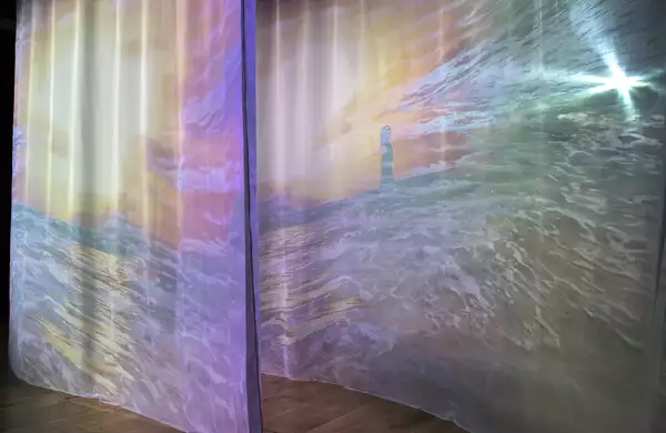 A photo of two transparent sheets of fabric hung in parallel curves with projections of waves on them