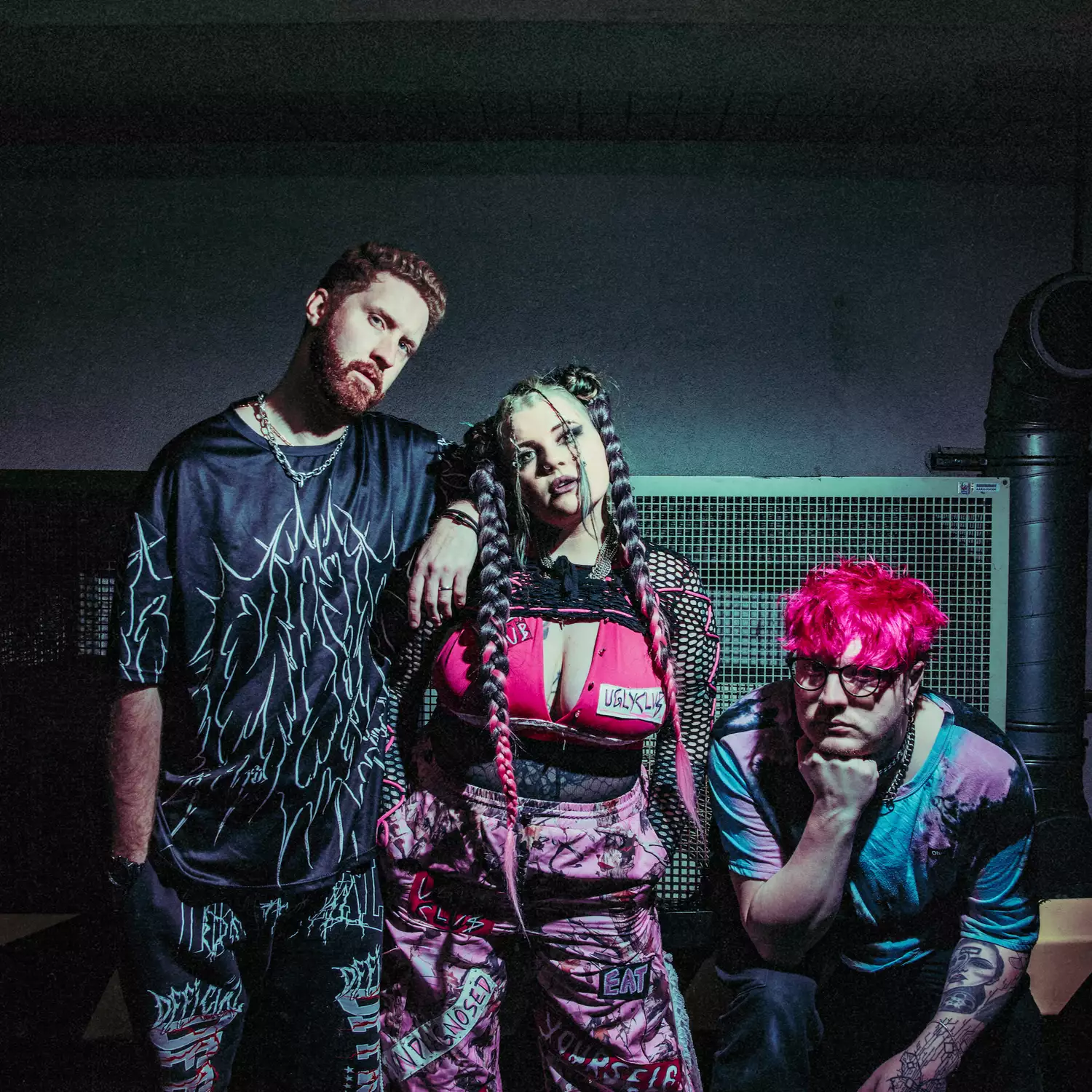 Three members of Ugly Club posing against a railing, wearing bright pink and blue clothing