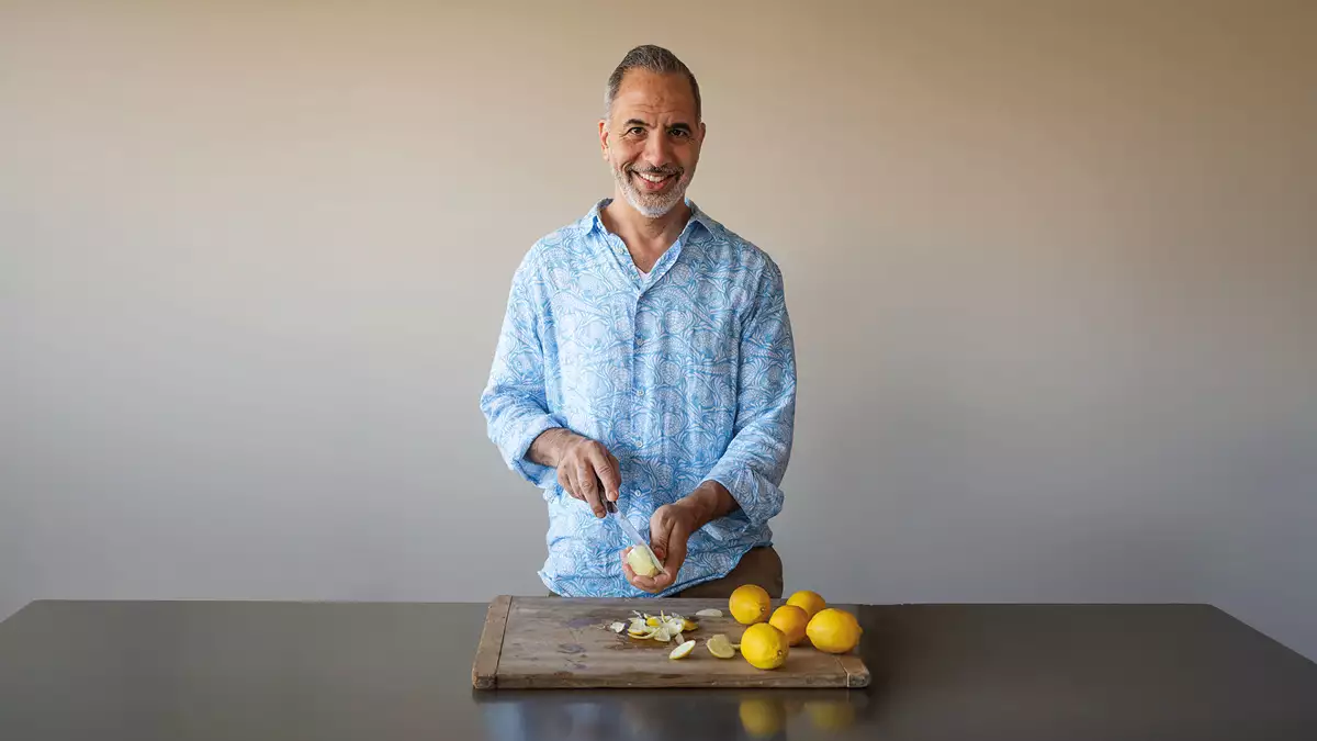 Yotam Ottolenghi wearing a light blue shirt cutting lemons on a wooden board