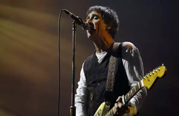 Johnny Marr on stage at Aviva Studios singing into a microphone and playing the guitar