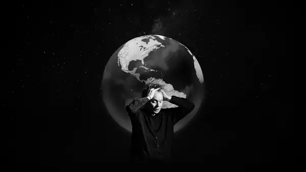 Black and white image of Laurie Anderson with her eyes closed and hands on her hand. Behind her is the earth.