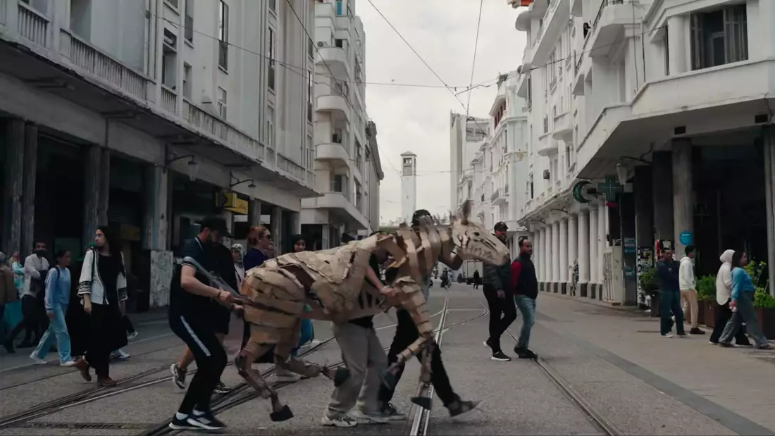 An animal puppet being led by puppeteers down a busy city street in Casablanca