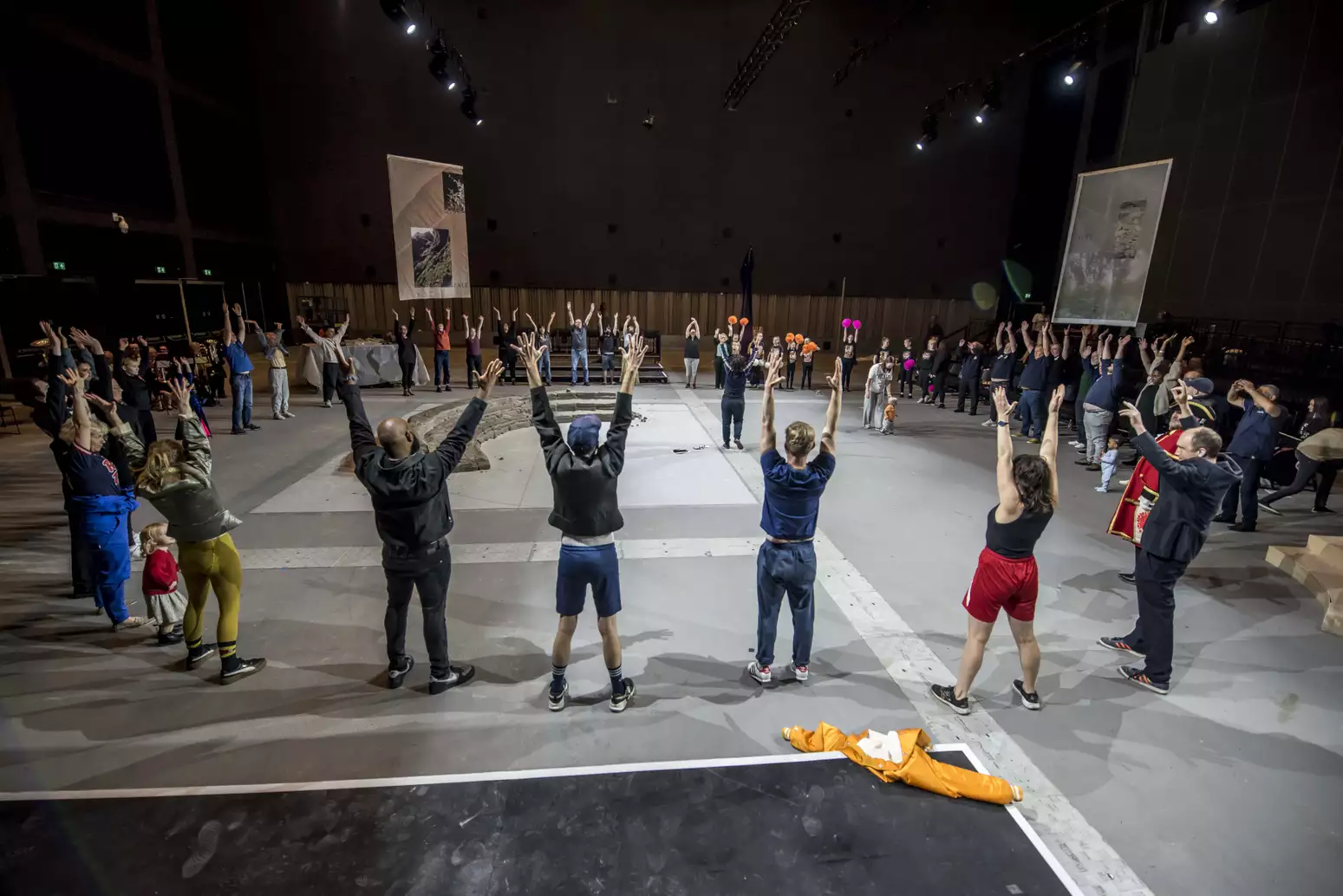 A large group of people with their hands in the air stood in a circle around a clay installation – for the June 2024 Artist Takeover