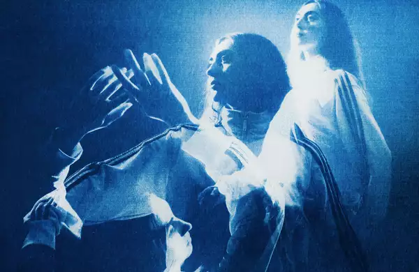 Person dancing with raised hands in blue light, with others behind them.