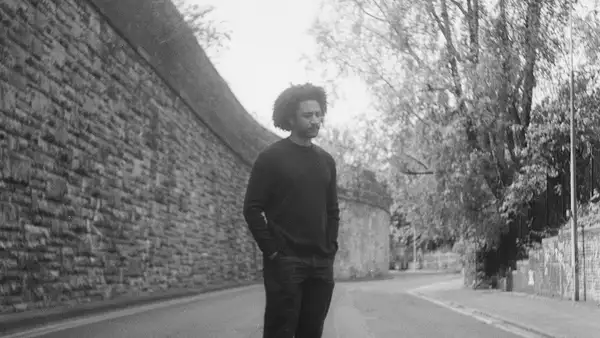 Black and white photo of Rory A Green stood on a deserted street next to a large wall