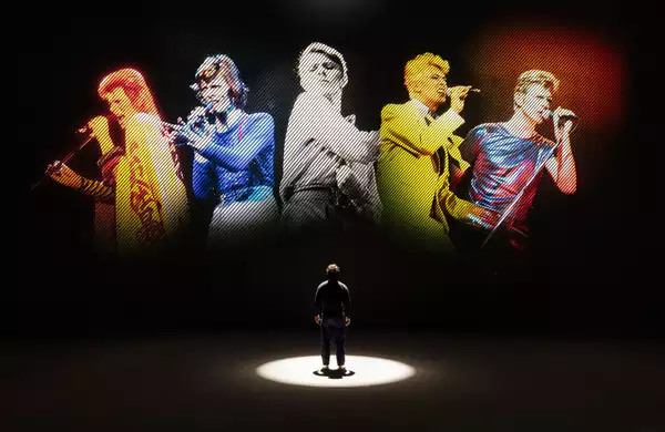A person looking at five versions of David Bowie singing on a large screen