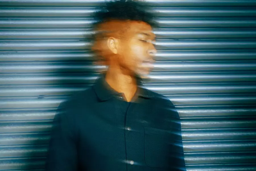 artist Obeka standing in front of a metal corrugated shutter looking wistfully to the side