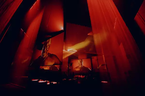 The set of A Symphony of Flesh and Bones in the Warehouse, showing projections on large screens and pieces of fabric. The screens show her father and the lighting is red.