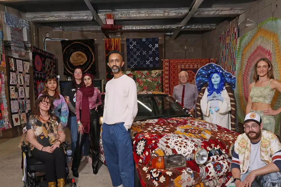 Hetain Patel standing in an exhibition with his artwork made from a car, with other people around him