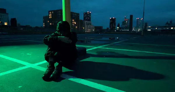 A person sat on a carpark roof at night, with a city skyline behind them