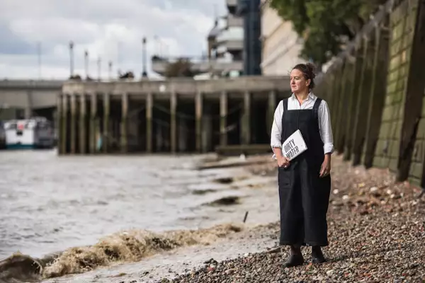 Tania Kovats stood besides some water holding a paper that says 'Dirty Water'
