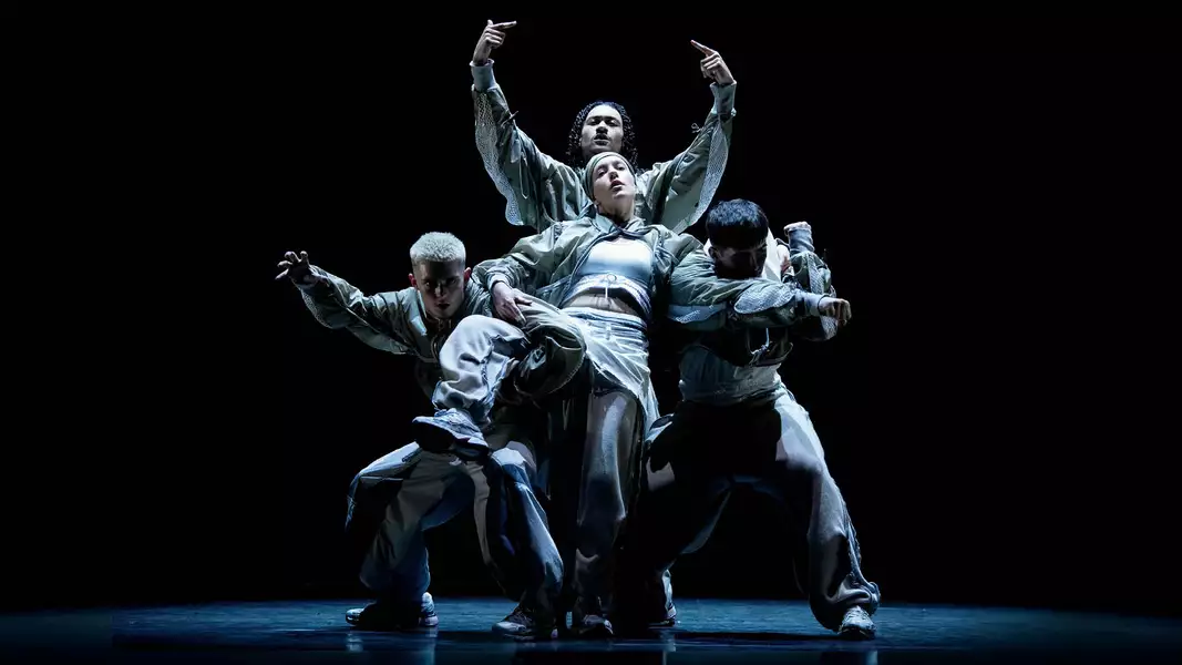 A group of five performers dancing on stage during CYCLES, dressed in loose-fitting, modern streetwear, against a dark background.
