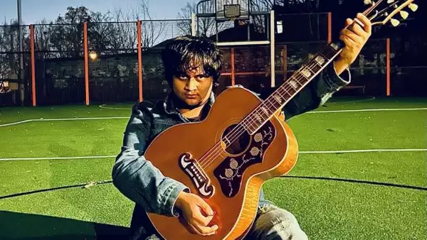 Photo of Zeny Bux playing guitar outside on a sports pitch