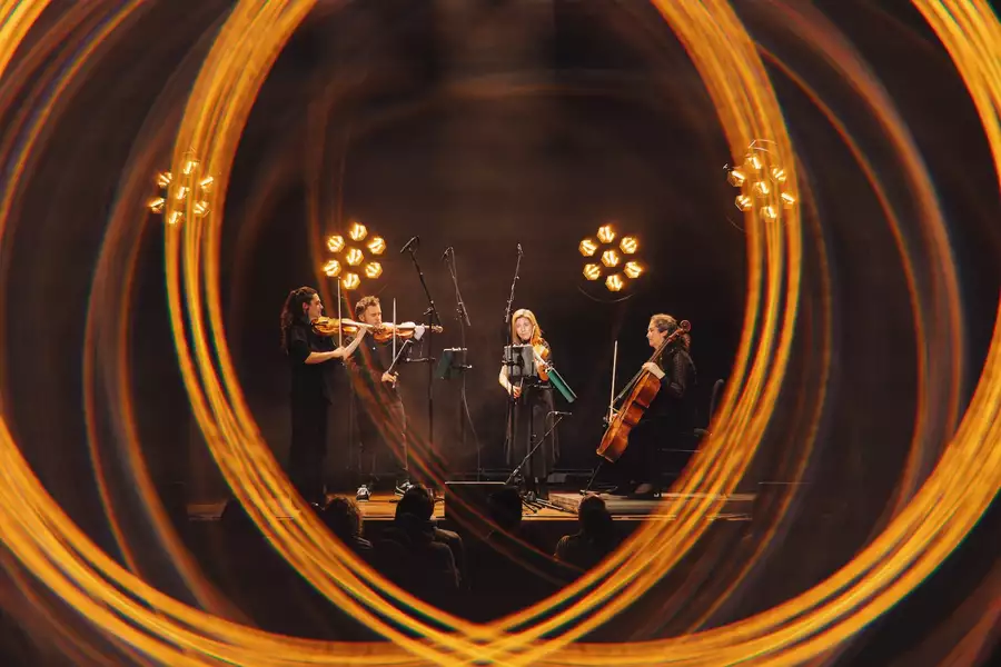 Four members of Manchester Collective perform on stage surrounded by blurred lighting