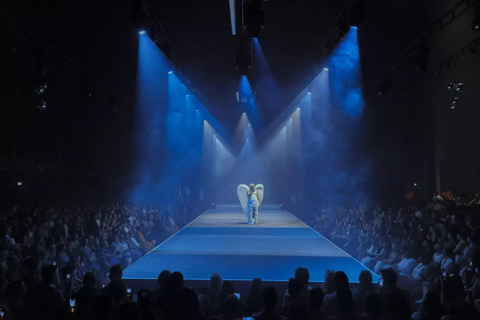A person dressed as an angel lit by spotlights on a runway